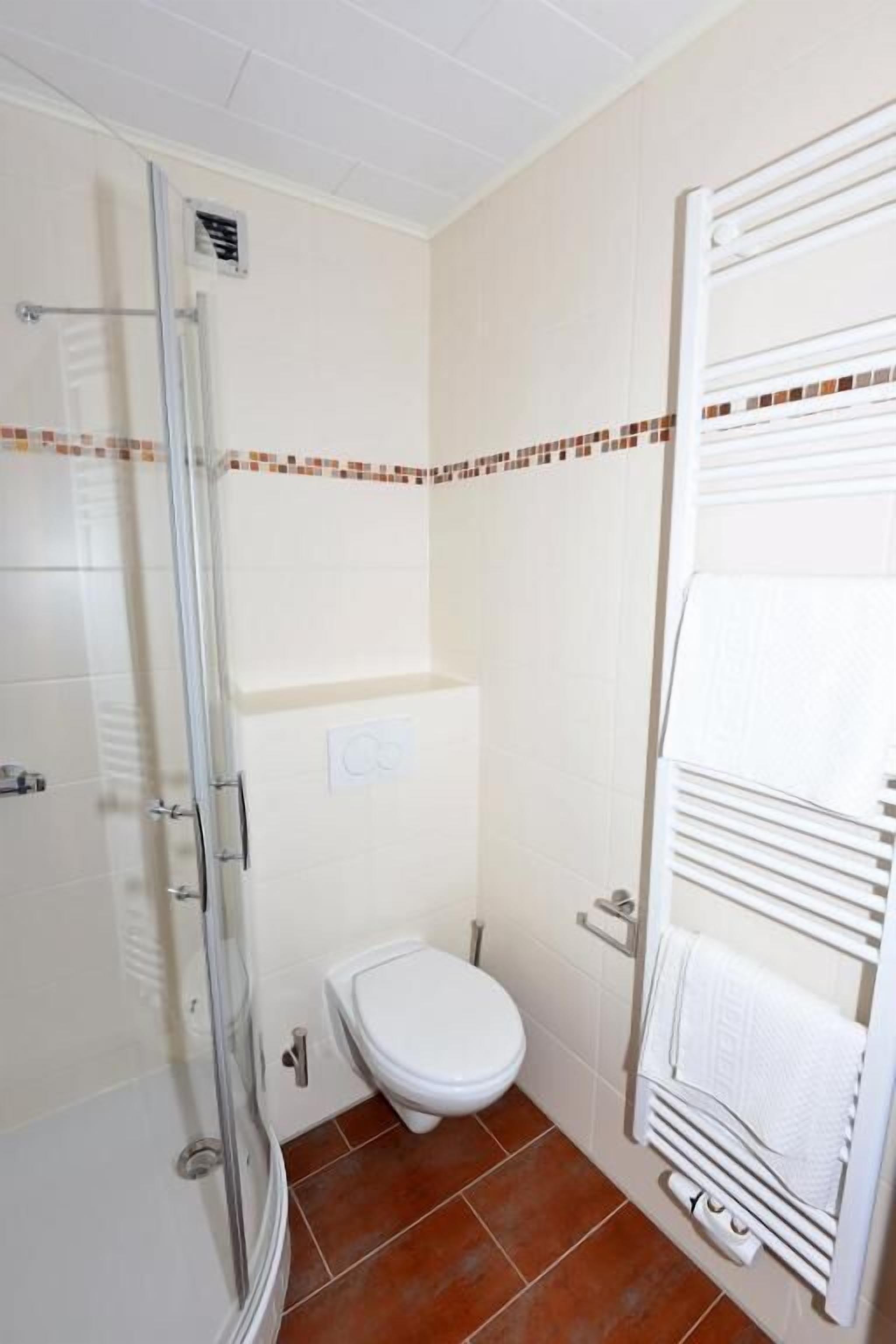 A bathroom with a glass shower enclosure, a toilet, and a towel rack.