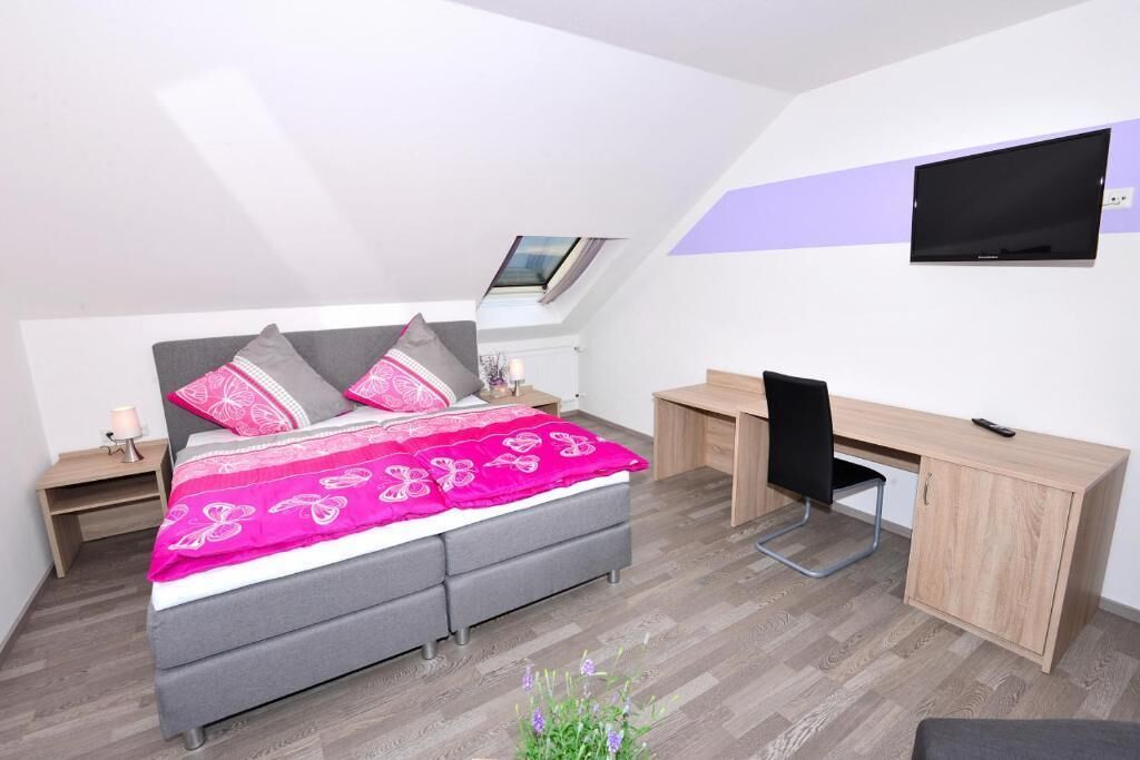 A bedroom with a bed, desk, chair, and a TV mounted on the wall.