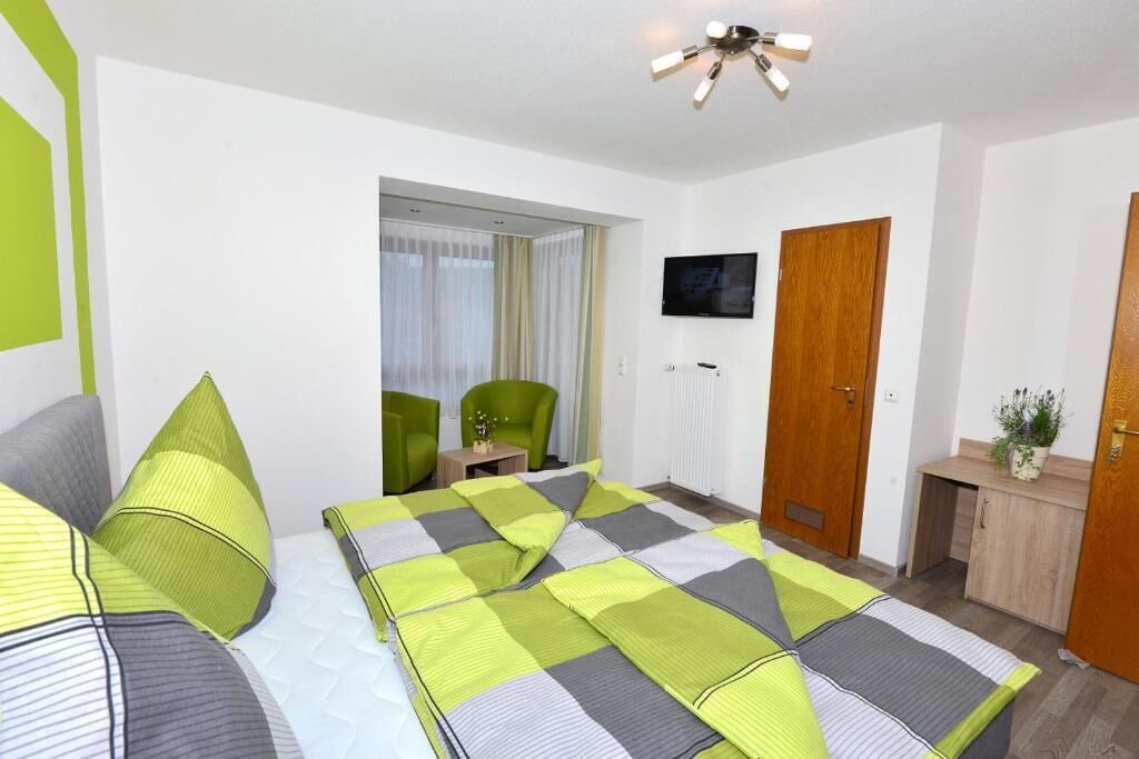 A hotel room with a bed, a desk, a chair, a television, and a door.