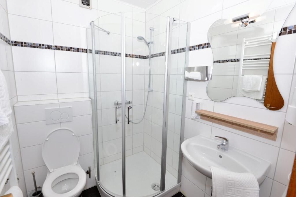 Ein modernes Badezimmer mit einer Duschkabine, einer weißen Toilette und einem Waschbecken mit Spiegel darüber.