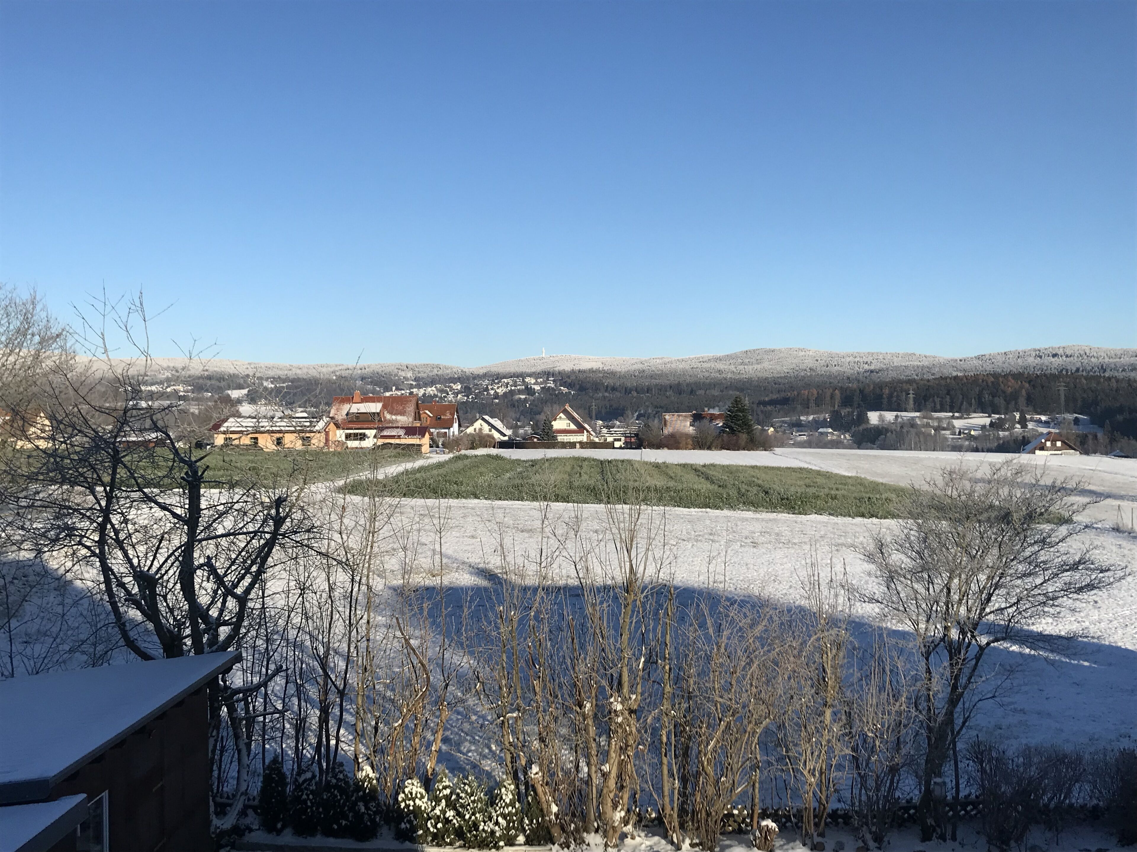 A rural landscape with snow-covered fields, a few houses, and a clear blue sky.