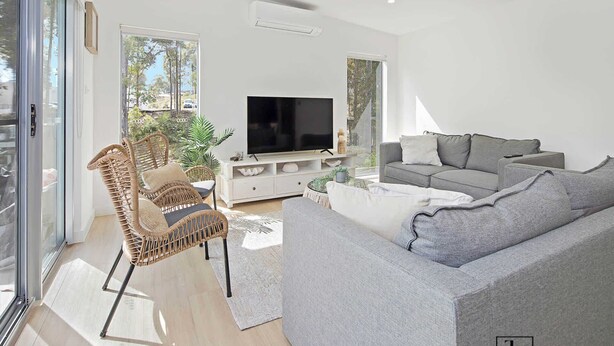En moderne stue med en grå sofa, en fletstol, et fladskærms-tv og et hvidt konsolbord.
