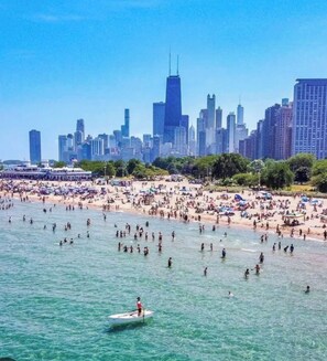 Una playa con gente nadando y un bote en el agua, y un horizonte urbano al fondo.