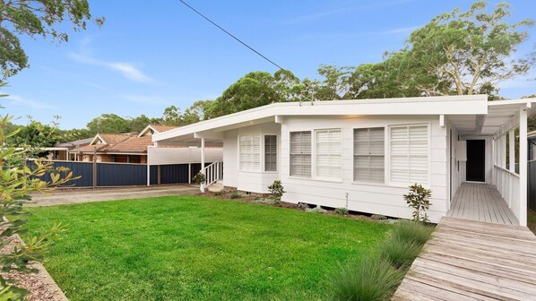 A white house with a covered porch, a fenced backyard, and a wooden deck.