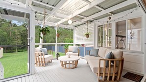A covered outdoor living area with wooden furniture, hanging plants, and string lights.