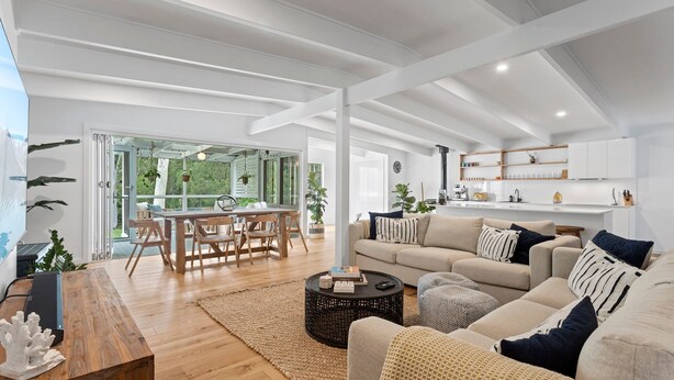 A spacious living room with a wooden dining table, a sofa set, and a kitchen area with white cabinets and a black stove.
