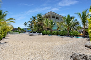 A building with a white car parked in front, surrounded by palm trees and gravel. - 5. Key Largo Waterfront Apartment | Reef & Relax (Key Largo)