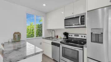 A modern kitchen with stainless steel appliances, a marble countertop, and a window with a view of greenery.