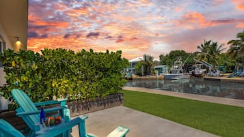 Une terrasse au bord de l’eau offrant une vue sur le coucher du soleil, une piscine et des chaises longues.