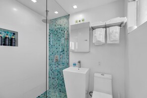 A modern bathroom with a glass shower enclosure, a white sink, and a toilet.
