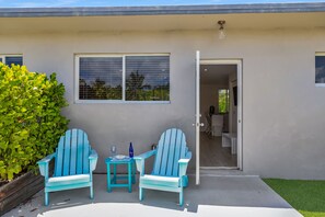 A house with a patio area featuring two blue Adirondack chairs, a small table, and a window with blinds. - 5. Key Largo Waterfront Apartment | Reef & Relax (Key Largo)