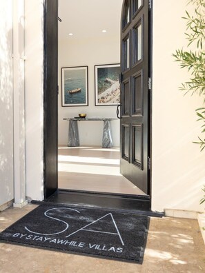 A hotel entrance with a black doormat reading "STAYAWHILE VILLAS" and a view into the interior featuring a marble countertop and framed artwork. - Chateau Beverly Hills by Stay Awhile Villas (Beverly Hills)