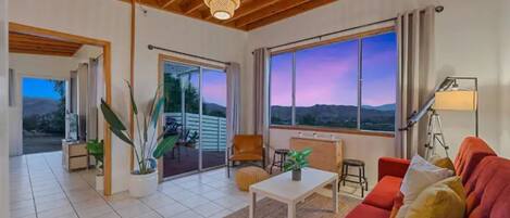 A spacious living room with a red sofa, a white coffee table, and a large window offering a view of the mountains.