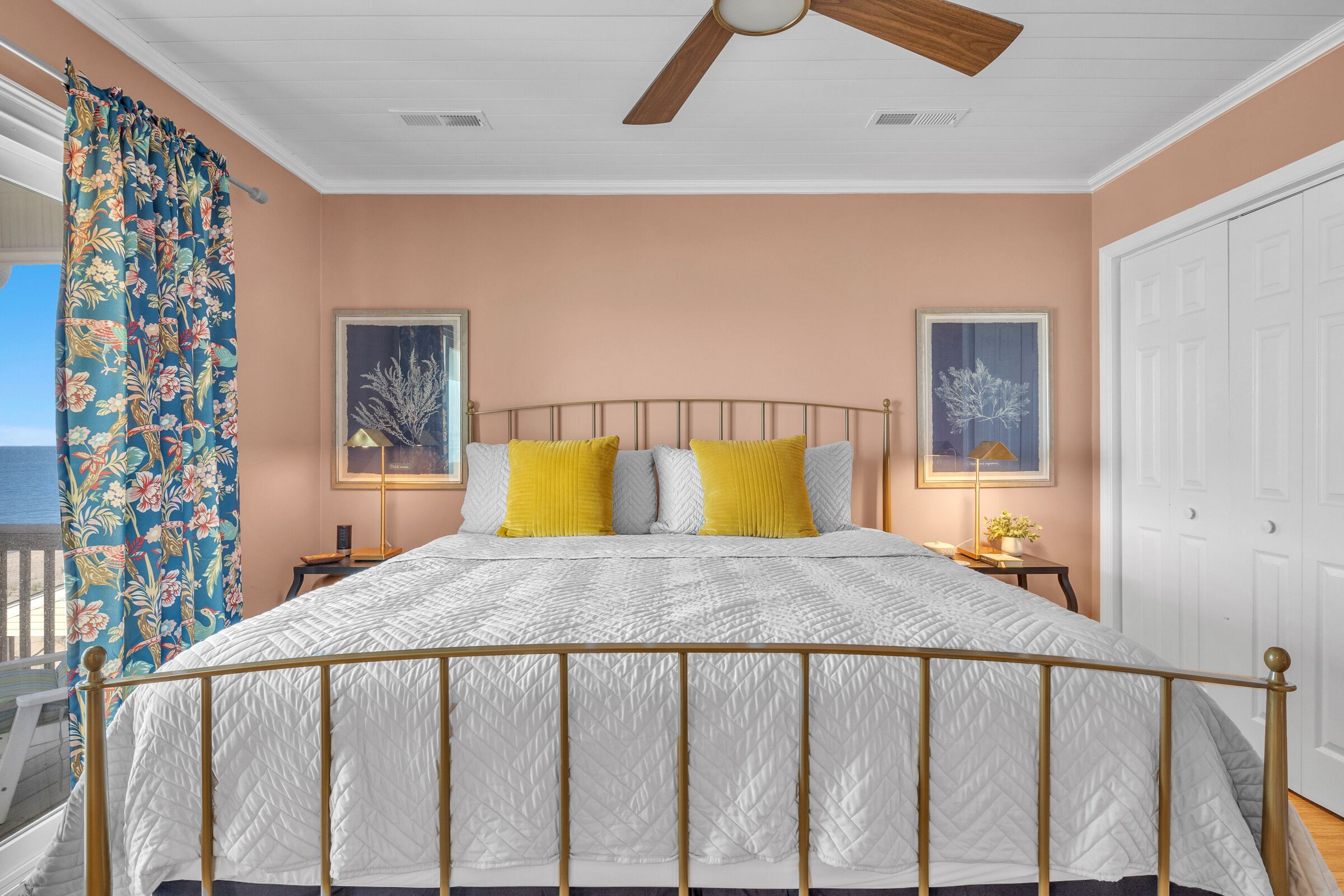 A bedroom with a bed, a ceiling fan, and two framed pictures on the wall.