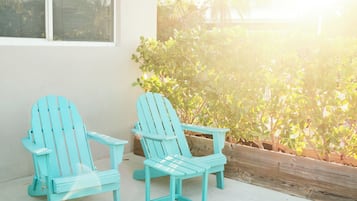 Twee lichtblauwe Adirondack-stoelen op een betonnen terras met uitzicht op een huis en tropische begroeiing.