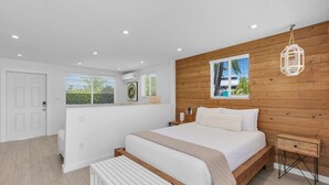 A modern bedroom with a wooden headboard, a bed with white bedding, a bedside table, and a view of the outdoors through the window. - 6. Key Largo Waterfront Studio / Dock / Snorkel (Key Largo)