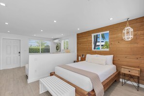 A modern bedroom with a wooden headboard, a bed with white bedding, a bedside table, and a view of the outdoors through the window. - 6. Key Largo Waterfront Studio / Dock / Snorkel (Key Largo)