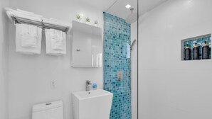 A bathroom with a white toilet, a sink, a mirror, and a shower with blue mosaic tiles. - 6. Key Largo Waterfront Studio | Dock, Snorkel (Key Largo)