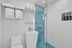 A bathroom with a white toilet, a sink, a mirror, and a shower with blue mosaic tiles. - 6. Key Largo Waterfront Studio | Dock, Snorkel (Key Largo)