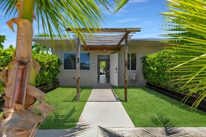 Ein modernes Haus mit einem Betonweg, der zum Eingang führt, umgeben von üppiger Vegetation und einer Holzpergola.