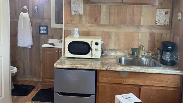 A compact kitchen with wooden cabinets, a microwave, a sink, and a refrigerator. - Delightful kitchenette style tiny home with loft. (Overton)