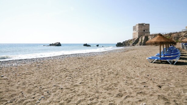 Una playa con una torre, piedras y una fila de sillas azules.