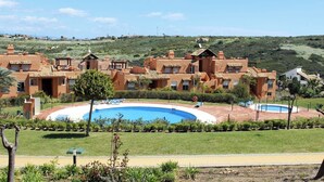 Un resort con varias edificaciones, una piscina central y un paisaje montañoso de fondo.