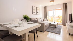 Una sala de estar moderna con comedor, sofá, televisor y balcón con mobiliario exterior.