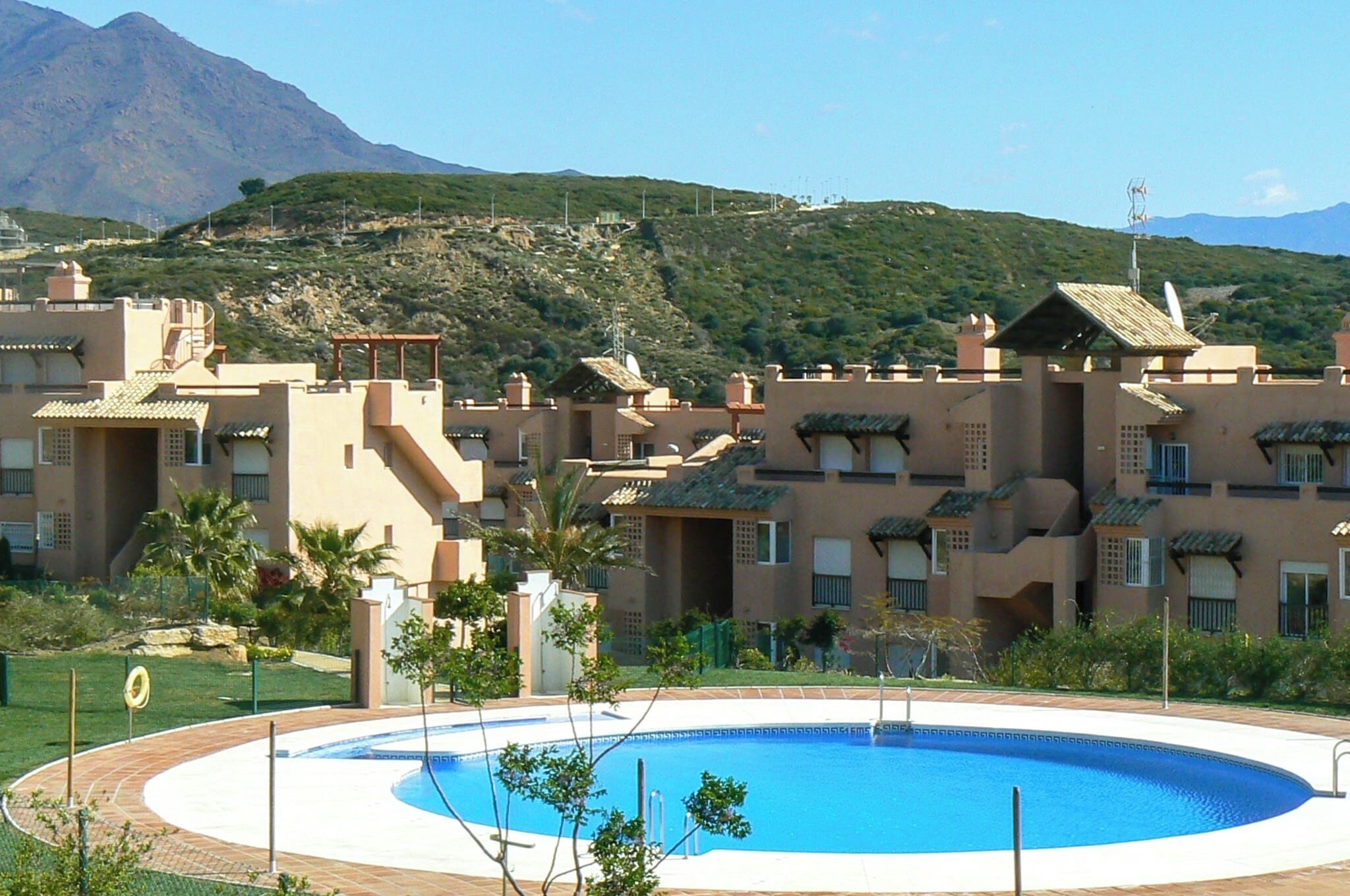 A resort with a swimming pool, multiple buildings with balconies, and a mountainous backdrop.