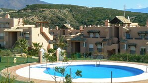 Un resort con piscina, varias edificaciones con balcones y montañas al fondo.