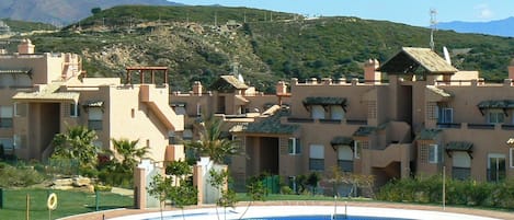 A resort with a swimming pool, multiple buildings with balconies, and a mountainous backdrop.