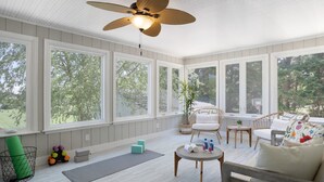 A sunroom with large windows, wicker furniture, and a ceiling fan.