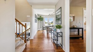 A hallway with a wooden staircase, a dining area with a table and chairs, and a kitchen area with a counter and cabinets.