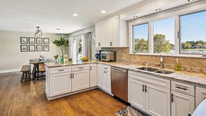A modern kitchen with white cabinets, a dishwasher, a microwave, and a large window with a view of trees and a lake.