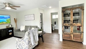 A living room with a grey sofa, a patterned armchair, a coffee table, and a wooden door with storage cabinets. - Quaint 2 bedroom cottage at Bass Lake-paddle boards, kayaks, private ramp, bikes (Knox)