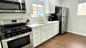 A kitchen with white cabinets, a stainless steel refrigerator, a microwave, and a stove. - Quaint 2 bedroom cottage at Bass Lake-paddle boards, kayaks, private ramp, bikes (Knox)