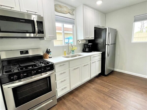 A kitchen with white cabinets, a stainless steel refrigerator, a microwave, and a stove.