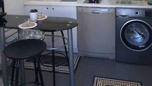 A compact kitchen with white cabinets, a stainless steel range hood, a dishwasher, and a washing machine.