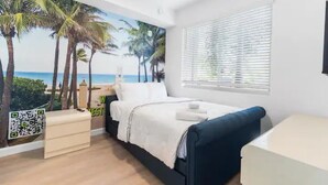 A bedroom with a bed, a nightstand, a desk, and a window with blinds. - Stylish & Cozy ~ 15mins to Downtown & Beach ~ Pool (West Palm Beach)