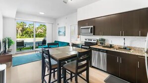 A modern kitchen with dark cabinets, a microwave, and a dishwasher. There is a dining area with a table and chairs, and a view of a green outdoor area through large sliding doors. - Stylish & Cozy ~ 15mins to Downtown & Beach ~ Pool (West Palm Beach)