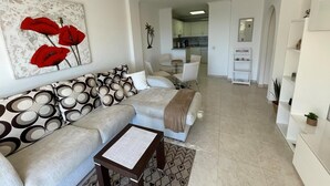 Een moderne woonkamer met een zithoek, een salontafel en een eethoek met een kleine tafel en stoelen. Achtergrond toont een keuken.