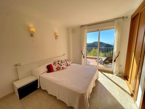 Een slaapkamer met een bed, een nachtkastje, een raam met uitzicht op het landschap en een deur.
