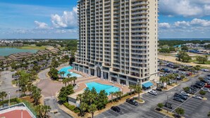 A high-rise hotel with multiple balconies, a swimming pool, and a parking lot.