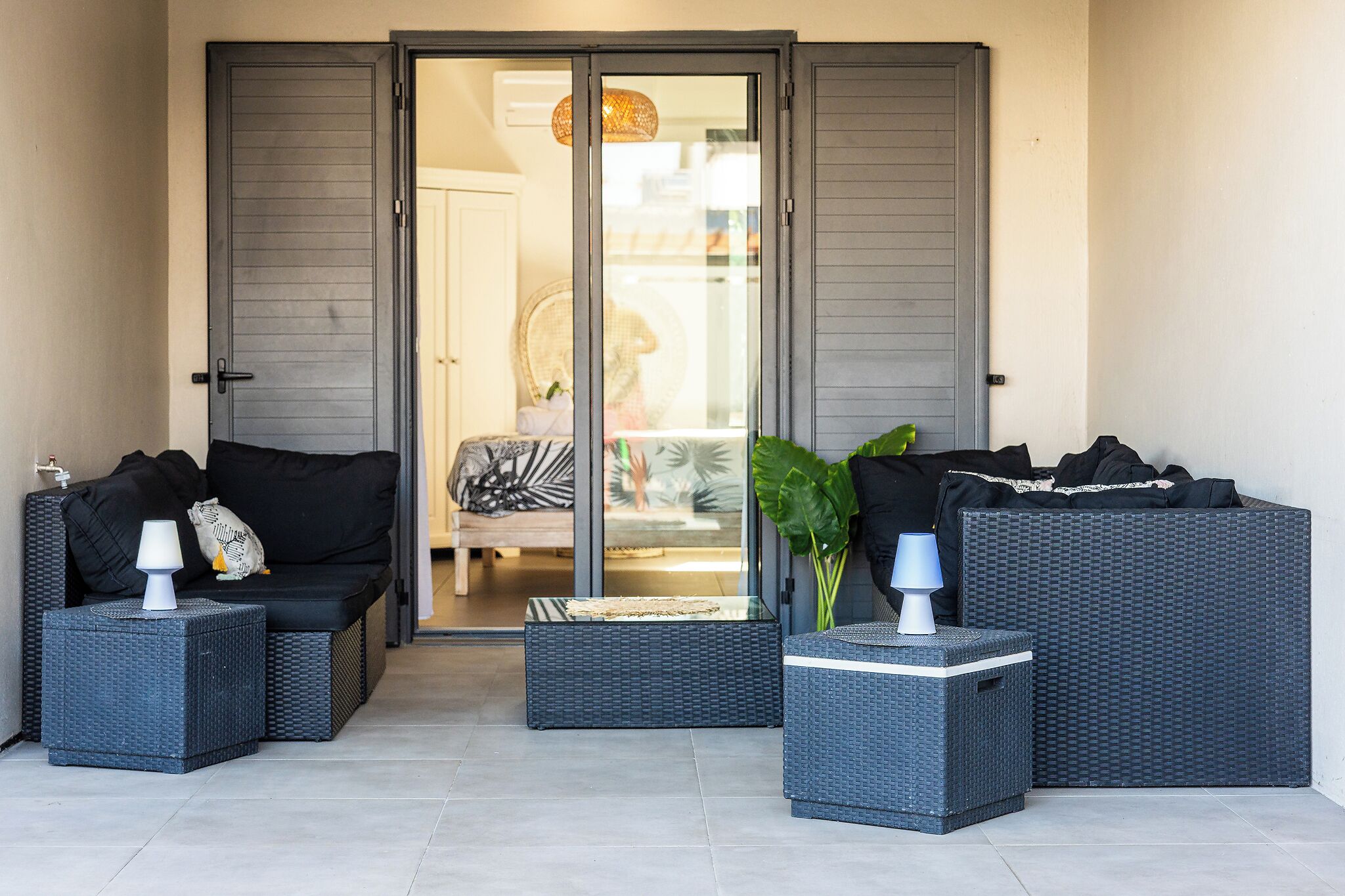 A patio area with wicker furniture, including a sofa and two side tables, and a glass door leading to an interior space.