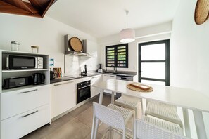 Une cuisine moderne avec des meubles blancs, un four à micro-ondes, une machine à café et un coin repas comprenant une table et des chaises blanches.