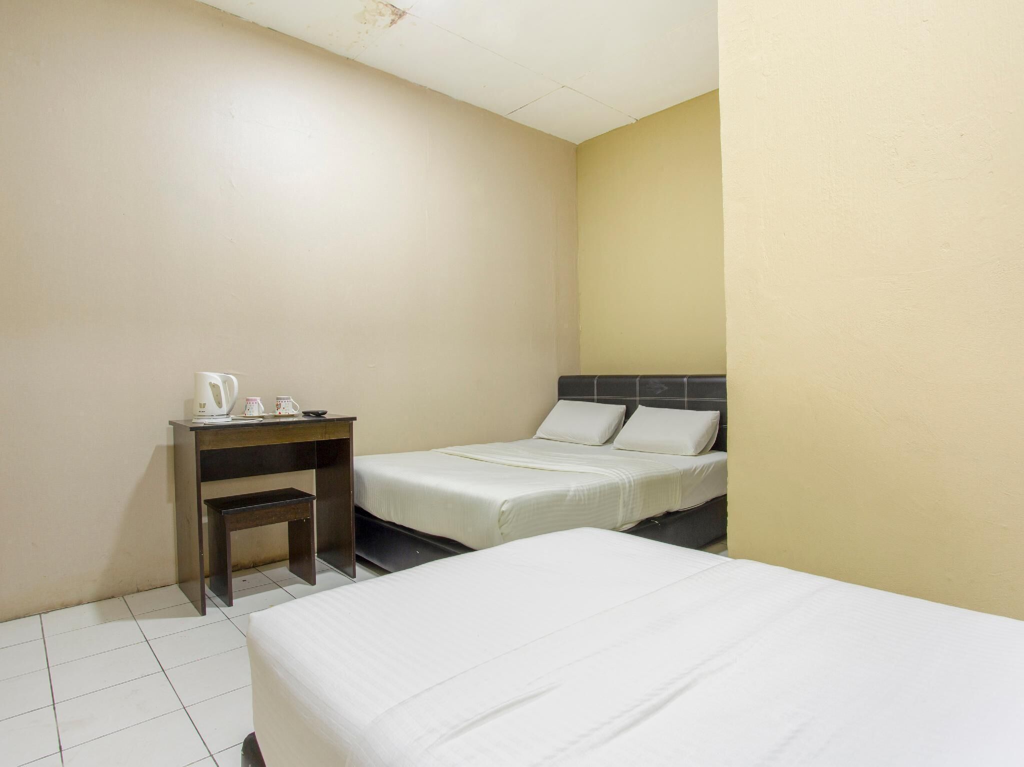 A hotel room with two beds, a small desk with a kettle, and a chair.