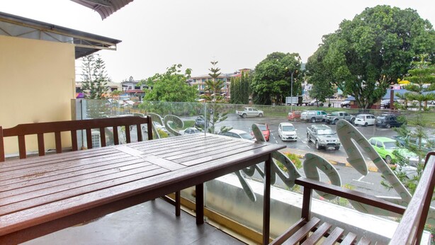A balcony with a wooden table and chairs, overlooking a busy street with cars and trees. - Lodge 37T (Ranau)