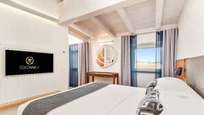 A modern hotel room with a large bed, a desk, a TV, and a view of the beach. - COLONNA24 (Portovenere)