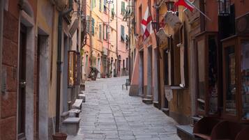 Una stretta strada acciottolata fiancheggiata da edifici, alcuni con balconi e tende da sole.
