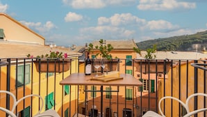 A terrace with a table set for two, a bottle of wine, and glasses. The terrace overlooks a cityscape with buildings and a hill in the distance. - COLONNA24 (Portovenere)